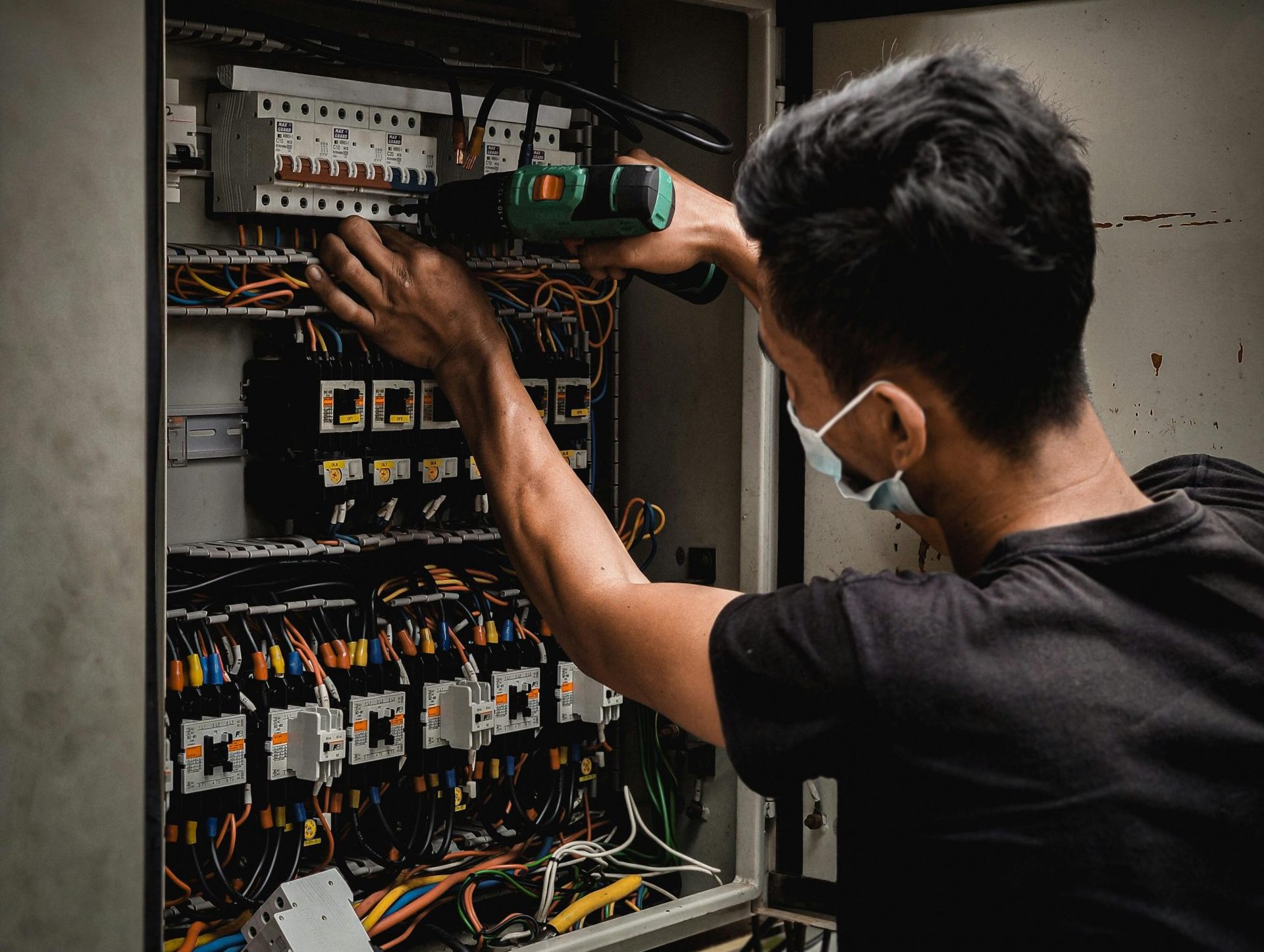 Technician working on circuit breaker panel, adjusting electrical wires indoors.