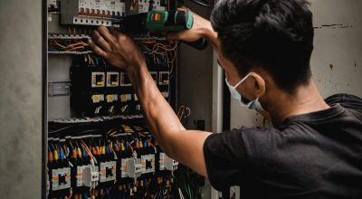 Technician working on circuit breaker panel, adjusting electrical wires indoors.